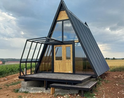 üçgen bungalov ev bir tarlanın ortasında duruyor , panaromik camlarıyla hem içeriden manzara gösterirken camdan gelen yansımalar bu bungalovun çevresini gösteriyor