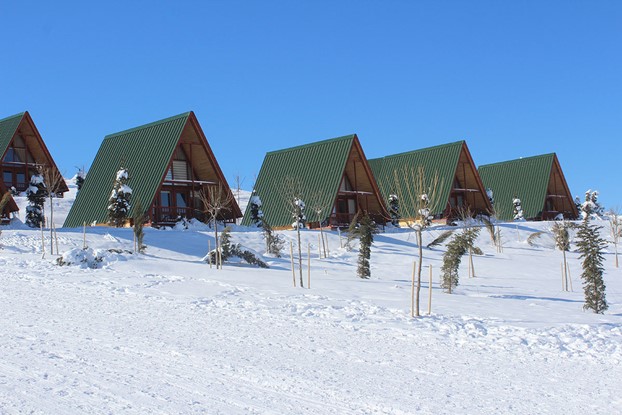 beş adet üçgen bungalov ev karlı bir arazide yan yana duruyor , çatı trapezleri yeşil renkte , bir bungalov kış turizm tesisi oteli için yapıldılar.. Turizm Tesisi tarzı Stella 70 evimiz Sivas, 'de inşa edildi.
